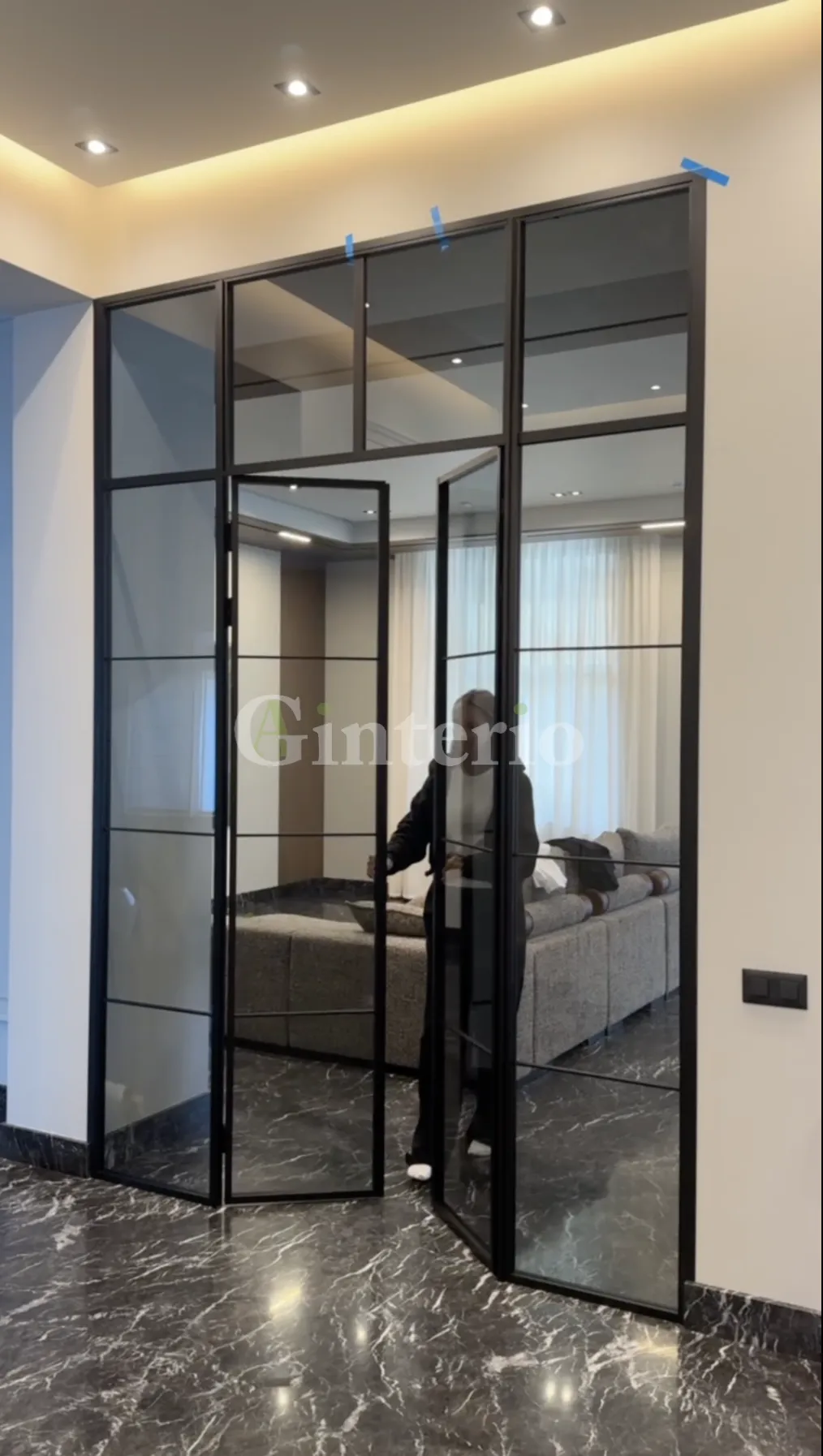 Девушка открывает двери распашной стеклянной перегородки, зонирующей гостиную. Купить, заказать межкомнатные перегородки